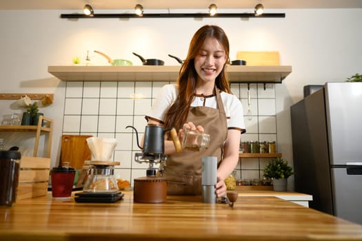 Happy woman in apron preparing pour over coffee at a wooden countertop.