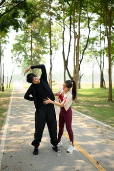Fit young couple stretching together before workout in park.