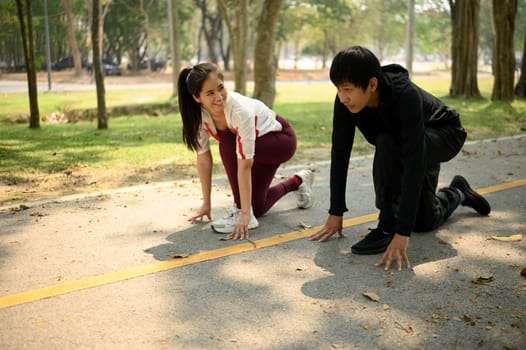 Young couple preparing to sprint in a park, crouched in starting position on a pathway.