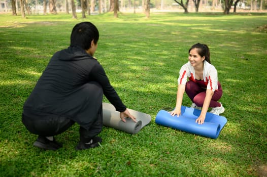 Young couple unrolling yoga mats on the grass in a sunny park. Healthy living concept.