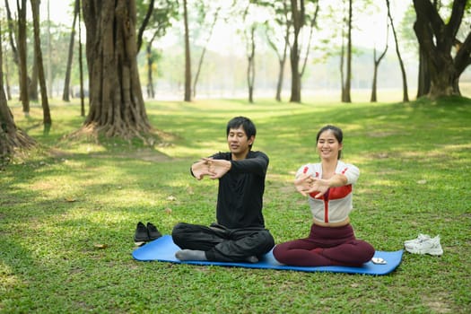 Young couple stretching on yoga mats in a peaceful park. Healthy lifestyle concept..