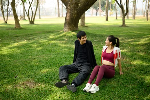 Happy fitness couple resting on grassy area in a park after workout. Healthy living concept.