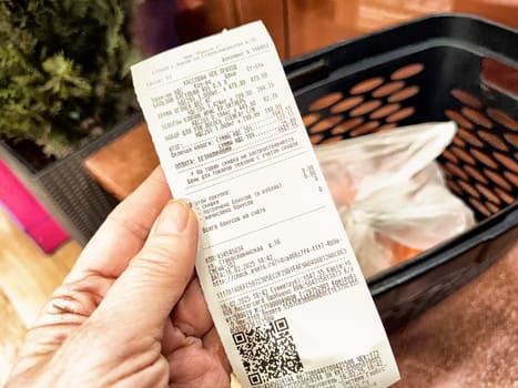 Kirov, Russia - February 14, 2025: A hand holds a detailed receipt from a grocery store, listing various items bought and their prices along with a QR code.
