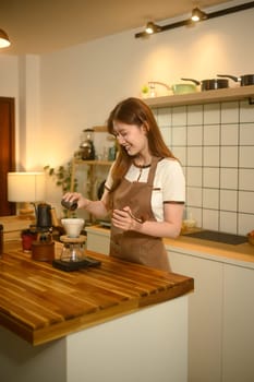 Happy woman in apron preparing pour over coffee at a wooden countertop.