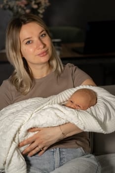 A mother cradles her baby in a soft blanket while sitting comfortably in a modern living room. The atmosphere is peaceful and serene, reflecting a close bond.