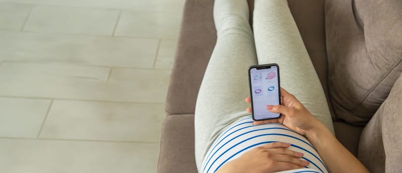 Pregnant woman on the phone in the online store for baby clothing. Selective focus. Cute.