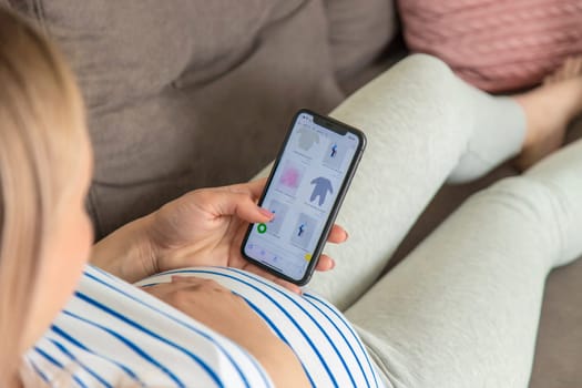 Pregnant woman on the phone in the online store for baby clothing. Selective focus. Cute.