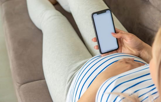 Pregnant woman on the phone in the online store for baby clothing. Selective focus. Cute.