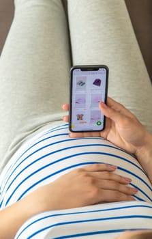 Pregnant woman on the phone in the online store for baby clothing. Selective focus. Cute.