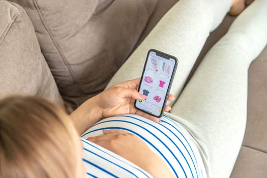 Pregnant woman on the phone in the online store for baby clothing. Selective focus. Cute.