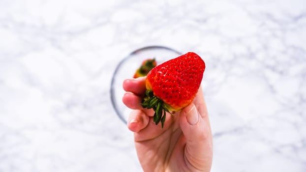 Flat lay. Strawberries, freshly washed and dried, are neatly stored in a glass bowl lined with a paper towel and securely covered with plastic wrap to maintain freshness.