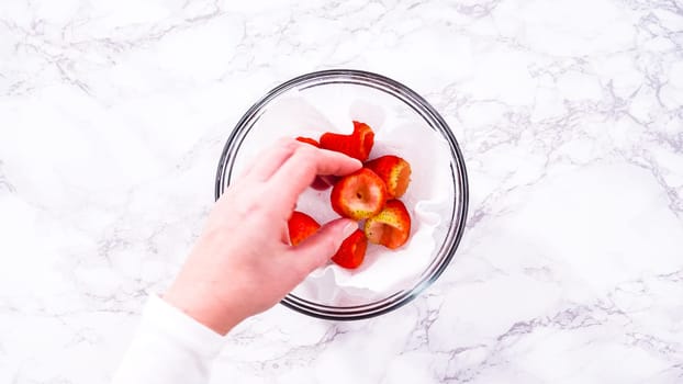 Flat lay. Strawberries, freshly washed and dried, are neatly stored in a glass bowl lined with a paper towel and securely covered with plastic wrap to maintain freshness.