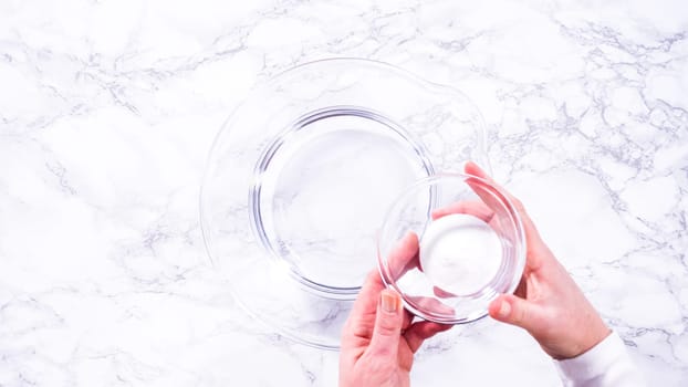 Flat lay. A spacious glass mixing bowl filled with water sits prepared to gently cleanse a batch of ripe strawberries, ensuring they are pristine before drying or storage.