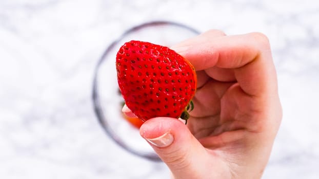 Flat lay. Strawberries, freshly washed and dried, are neatly stored in a glass bowl lined with a paper towel and securely covered with plastic wrap to maintain freshness.