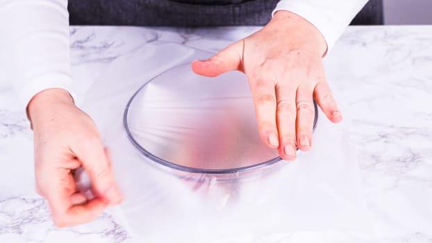 Strawberries, freshly washed and dried, are neatly stored in a glass bowl lined with a paper towel and securely covered with plastic wrap to maintain freshness.