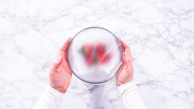 Flat lay. Strawberries, freshly washed and dried, are neatly stored in a glass bowl lined with a paper towel and securely covered with plastic wrap to maintain freshness.