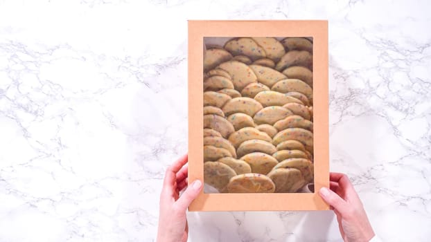 Flat lay. With precision, the woman is carefully arranging the sugar cookies, filled with dough-mixed sprinkles, into a rustic brown paper box.