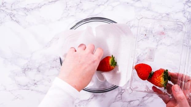 Flat lay. Freshly washed and dried strawberries are carefully arranged in a glass bowl lined with paper towel, ready for snacking or further use.