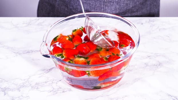 Ripe strawberries are submerged in water within a large glass mixing bowl, a step in washing the fruit to ensure cleanliness and longevity before storage or consumption.