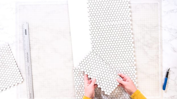 Flat lay. In the process of mounting peel and stick mosaic tiles onto a foam board, perfect for enhancing a food photography studio's aesthetic.