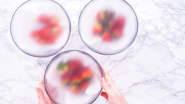 Flat lay. Strawberries, freshly washed and dried, are neatly stored in a glass bowl lined with a paper towel and securely covered with plastic wrap to maintain freshness.