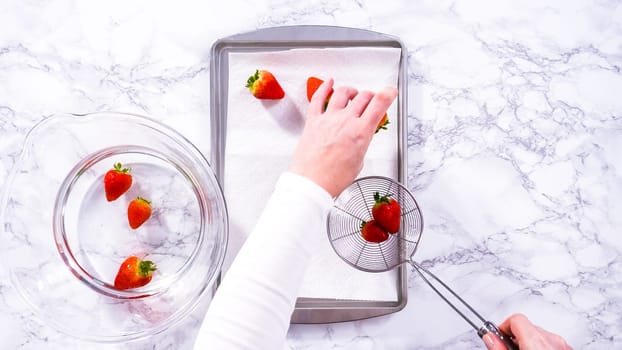 Flat lay. Juicy red strawberries, freshly washed, are spread out to dry on a baking sheet, carefully lined with paper towels to absorb excess moisture and prevent mold.