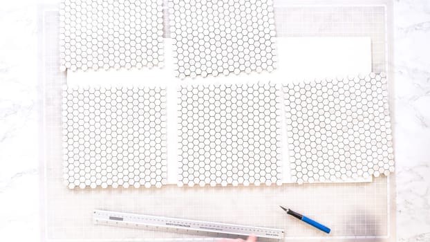 Flat lay. In the process of mounting peel and stick mosaic tiles onto a foam board, perfect for enhancing a food photography studio's aesthetic.