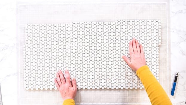 Flat lay. In the process of mounting peel and stick mosaic tiles onto a foam board, perfect for enhancing a food photography studio's aesthetic.