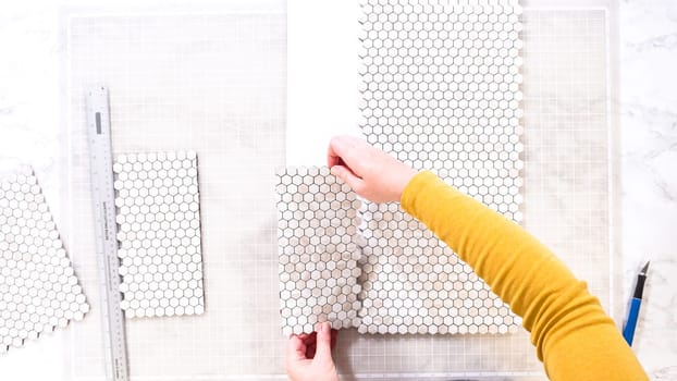 Flat lay. In the process of mounting peel and stick mosaic tiles onto a foam board, perfect for enhancing a food photography studio's aesthetic.