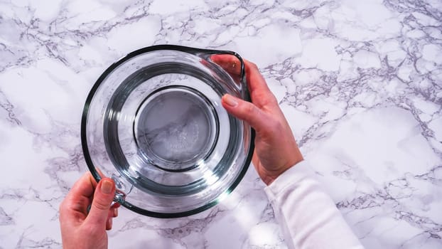 Flat lay. A spacious glass mixing bowl filled with water sits prepared to gently cleanse a batch of ripe strawberries, ensuring they are pristine before drying or storage.