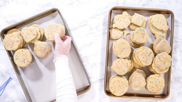 Flat lay. With precision, the woman is carefully arranging the sugar cookies, filled with dough-mixed sprinkles, into a rustic brown paper box.