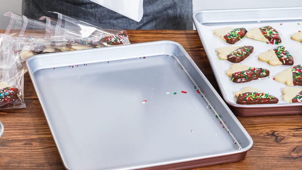 Carefully packaging Christmas cutout cookies, half-dipped in chocolate and presented in clear cellophane wrapping, perfect for festive gifting.