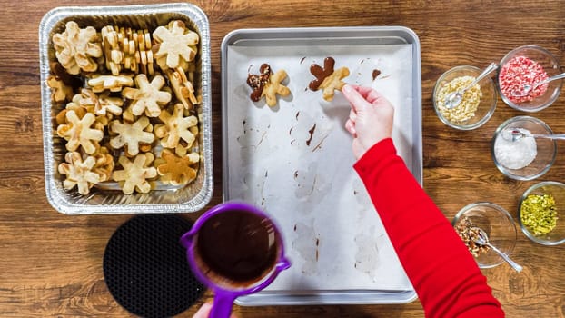 Flat lay. Creating snowflake-shaped cutout sugar cookies, dipped in chocolate, and adorned with different toppings.