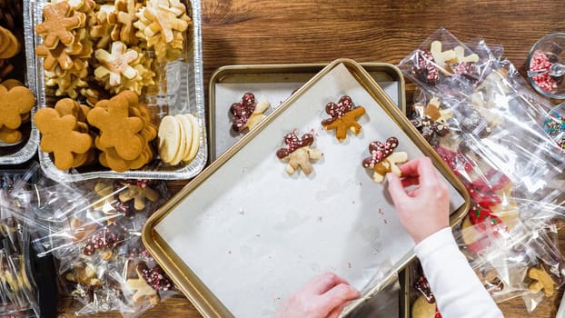 Flat lay. Carefully packaging Christmas cutout cookies, half-dipped in chocolate, sprinkled with crushed nuts, and presented in clear cellophane wrapping.