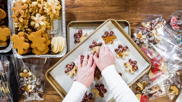 Flat lay. Carefully packaging Christmas cutout cookies, half-dipped in chocolate, sprinkled with crushed nuts, and presented in clear cellophane wrapping.