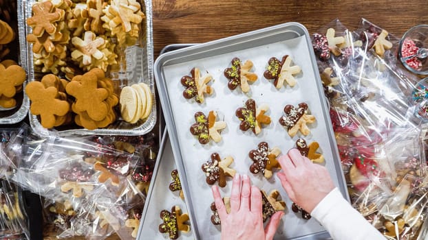 Flat lay. Carefully packaging Christmas cutout cookies, half-dipped in chocolate, sprinkled with crushed nuts, and presented in clear cellophane wrapping.
