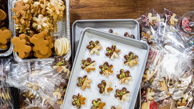 Flat lay. Carefully packaging Christmas cutout cookies, half-dipped in chocolate, sprinkled with crushed nuts, and presented in clear cellophane wrapping.