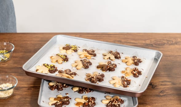 Creating snowflake-shaped cutout sugar cookies, dipped in chocolate, and adorned with crushed pecan nuts, elegantly presented on parchment.