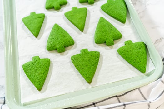 Freshly baked Green Gingerbread Cookies in tree shapes arranged on a baking tray lined with parchment paper, ready for cooling and display.