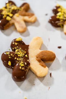 Crafting star-shaped holiday cookies dipped in chocolate and sprinkled with crushed pistachios, arranged on parchment paper.