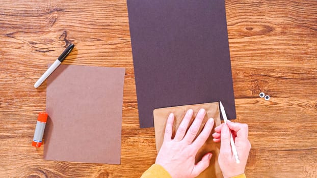 Step by step. Flat lay. Teacher guides online class through making a paper puppet from a brown bag, creatively using a wooden surface as a workspace.