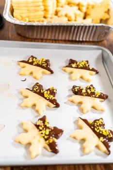 Crafting star-shaped holiday cookies dipped in chocolate and sprinkled with crushed pistachios, arranged on parchment paper.