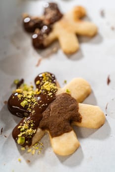 Crafting star-shaped holiday cookies dipped in chocolate and sprinkled with crushed pistachios, arranged on parchment paper.