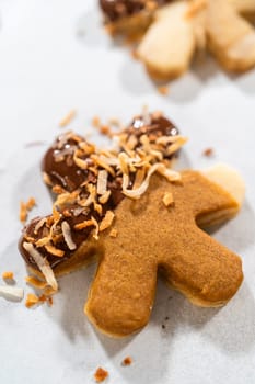 Gingerbread men cookies, chocolate-dipped feet, generously sprinkled with golden toasted coconut shavings, artfully arranged on parchment paper.