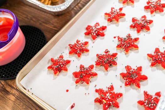Vivid red star-shaped cookies, generously iced and speckled with green and white holiday sprinkles, freshly prepared and laid out to dry.