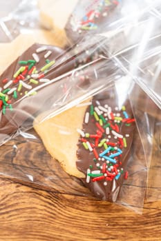 Carefully packaging Christmas cutout cookies, half-dipped in chocolate and presented in clear cellophane wrapping, perfect for festive gifting.