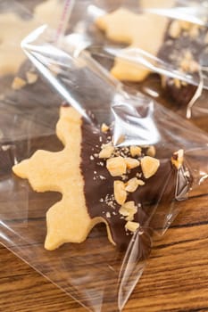 Carefully packaging Christmas cutout cookies, half-dipped in chocolate and presented in clear cellophane wrapping, perfect for festive gifting.