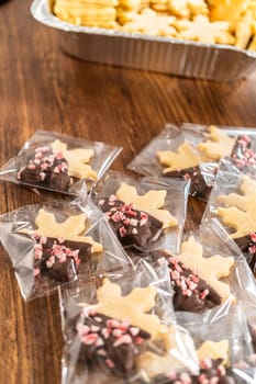 Carefully packaging Christmas cutout cookies, half-dipped in chocolate and presented in clear cellophane wrapping, perfect for festive gifting.