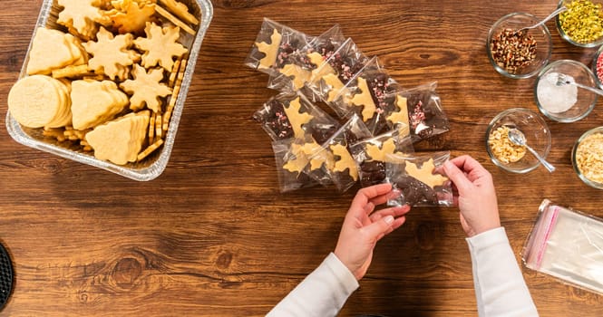 Carefully packaging Christmas cutout cookies, half-dipped in chocolate and presented in clear cellophane wrapping, perfect for festive gifting.