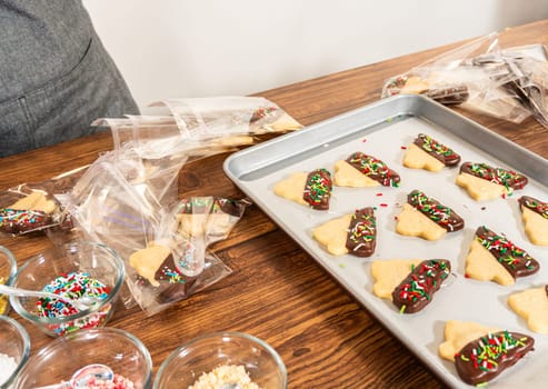 Carefully packaging Christmas cutout cookies, half-dipped in chocolate and presented in clear cellophane wrapping, perfect for festive gifting.
